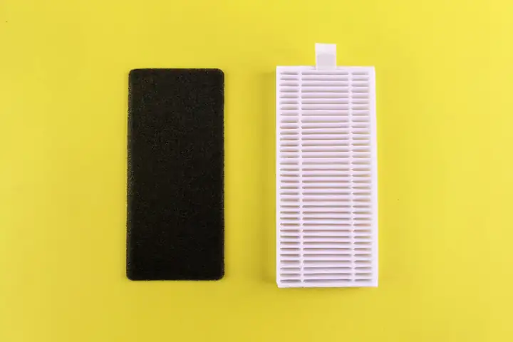 Black foam filter pad lying next to a white pleated filter on a yellow background