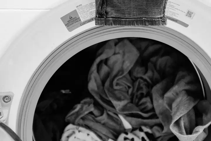 Damp clothes piled inside a front-load machine drum, jeans hanging over the door