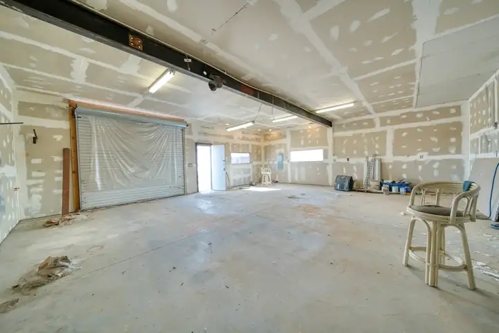 Unfinished room with taped and mudded drywall, a concrete floor and a plastic-covered roll-up door