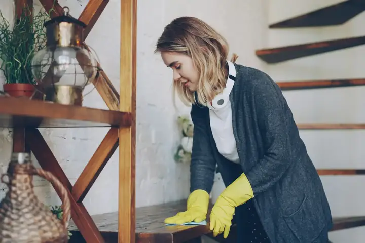 Person in yellow gloves wiping dust from a wooden surface with a cloth