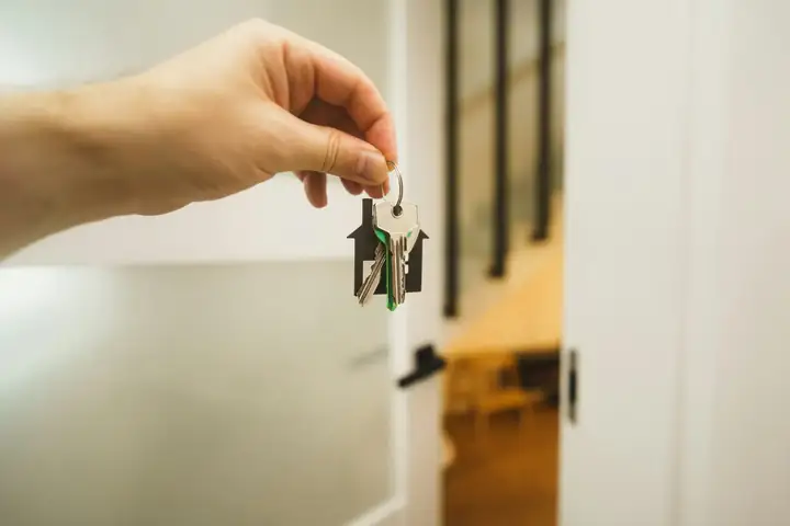 Hand holding a house key up to the lock of a front door
