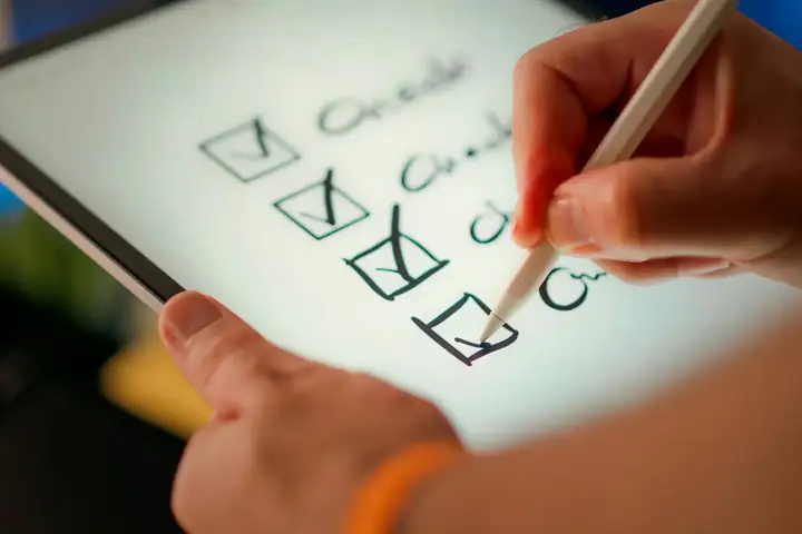 Hand holding a stylus and ticking items off a checklist on a tablet screen